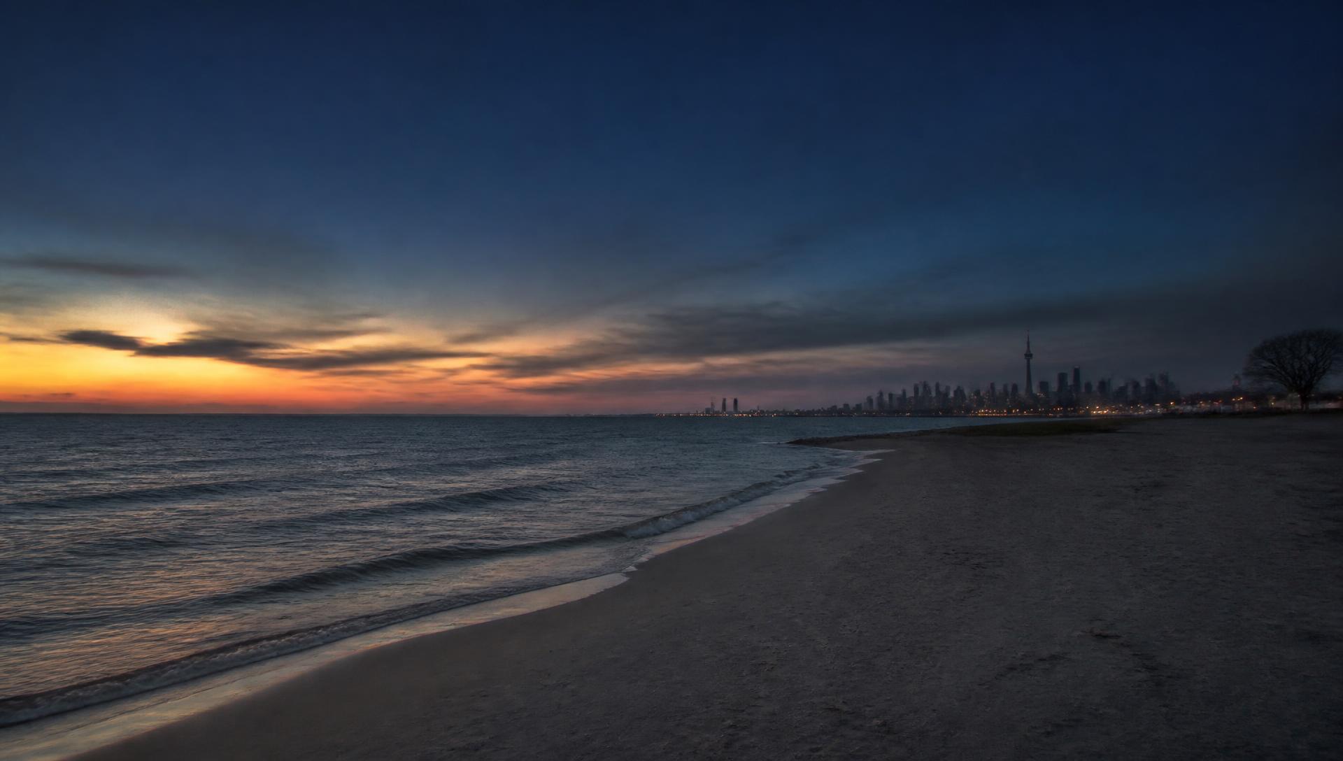 Lake Ontario shoreline at dusk with the Toronto skyline in the distance